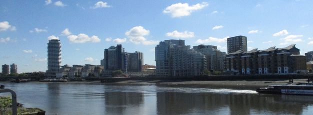 Buildings and housing across a rippling river stand against a blue sky.