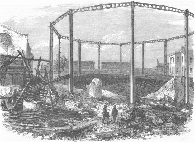 Print. The walls of a polygonal building have been blasted away by an explosion that blackened some of the structures nearby. Two men look at the damage at the bottom centre of the engraving.